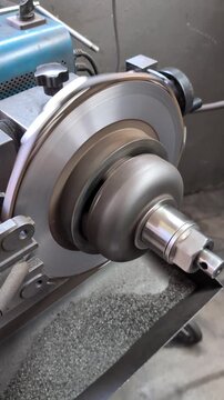 Professional lathe machine skimming a car's brake disc rotor during a vehicle repair service, with the rotating metal part creating fine shavings that fall into a collection tray