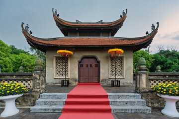 Fototapeta premium Traditional Vietnamese architecture of North Gate Cua Bac, Imperial Citadel of Thang Long, Hanoi, Vietnam. Featuring red tiled roof, ornate details, a welcoming red carpet, and vibrant yellow flowers