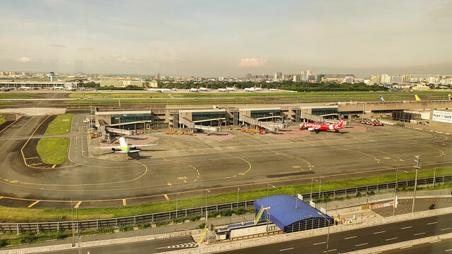 Manila, Philippines - May 15, 2025: View of Ninoy Aquino International Airport terminal and aircraft parking area in Manila with AirAsia airplanes, taxiways and urban skyline under sunny sky.