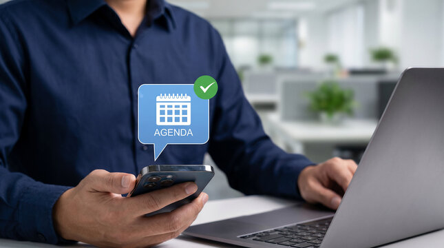 Corporate employee using mobile calendar app next to laptop for appointment and meeting planning