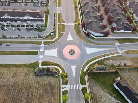Looking down from a drone point of view at a suburban neighborhood with a round-about at the intersection of two roads.