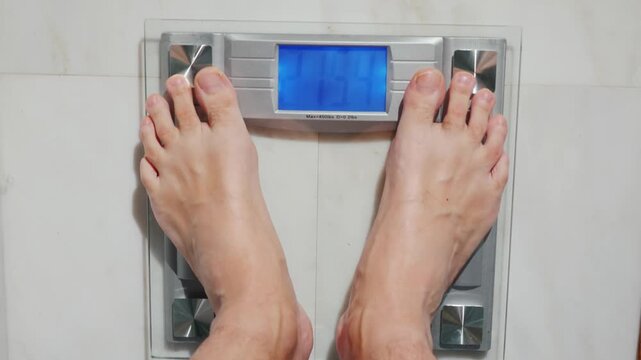 Man steps onto bathroom scale showing weight 215.4 lbs or 97.7 kg motion footage.