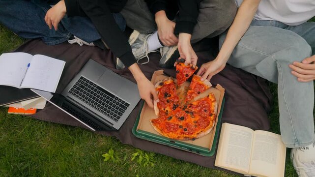 Top down close up of hands taking pizza slices from box on blanket