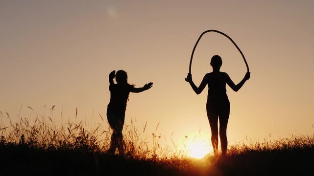 Silhouettes of children exercising outdoors at sunset playing jumping rope and doing cartwheels.