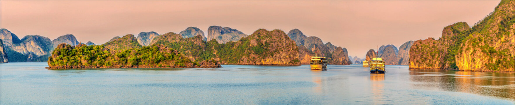 A panorama view of Karst limestone islets and cruise ships in the glow of the setting sun in Ha Long Bay, Vietnam close to sunset