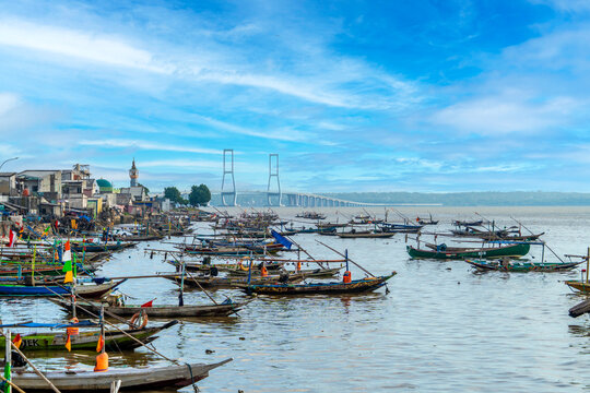 Colorful fishing boats docked at Bulak fisherman&rsquo;s beach with the famous Suramadu Bridge in the background, linking Java and Madura Islands. Beautiful seascape in Surabaya, Indonesia.