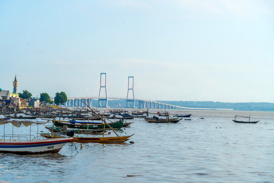 Colorful fishing boats docked at Bulak fisherman&rsquo;s beach with the famous Suramadu Bridge in the background, linking Java and Madura Islands. Beautiful seascape in Surabaya, Indonesia.