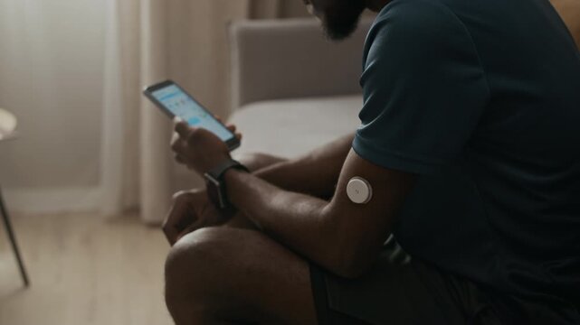 Side view shot of unrecognizable young adult Black man monitoring blood sugar via app linked to wearable CGM device on upper arm during everyday diabetes care, slow motion
