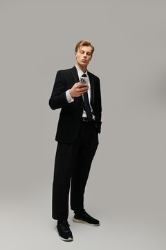 Stylish young man in sharp suit looking at his phone against a neutral backdrop