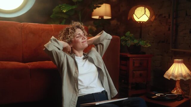 Happy curly haired woman stretching with relief after finishing remote work on laptop at home. High quality 4k footage