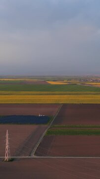 Solar power plant and photovoltaic panels in colorful agricultural fields with high voltage power lines, Vertical 9x16 format, Aerial lateral right to left reveal, 4K