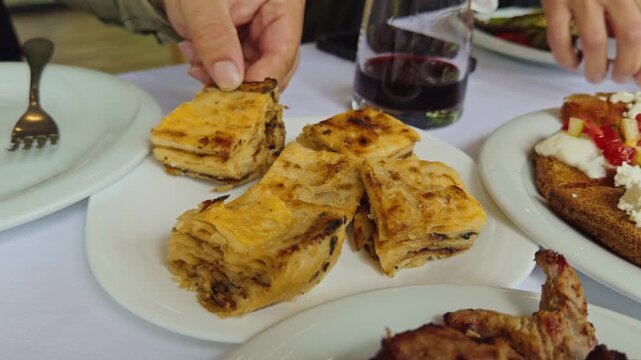 Cinematic close-up of traditional Albanian fli served on a dining table with wine, grilled meat, and Mediterranean dishes.