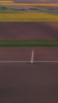 High voltage electricity pylons glowing in red sunset light over minimalist agricultural fields, Vertical 9x16 format, High altitude aerial lateral flight, 4K