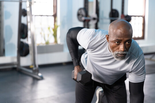 Senior African American man performing leaning row in gym, holding hex dumbbell, wearing sportswear