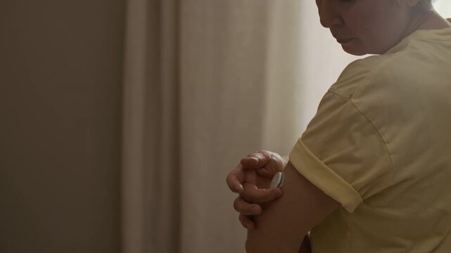 Close up shot of senior woman adjusting CGM patch attached to upper arm while using wearable device for diabetes care at home, slow motion