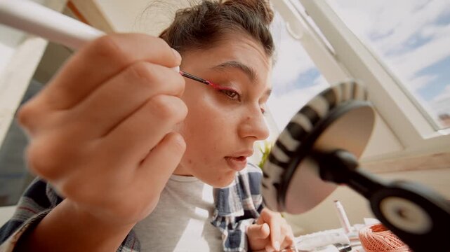 Focused woman carefully applying eyeliner in detailed reflection