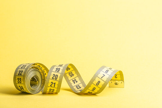 Measuring tape on yellow background displays numbers for diet and fitness tracking