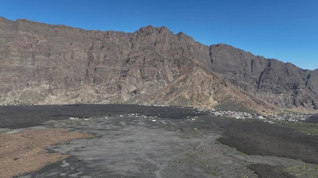 Aerial panoramic of the dramatic Fogo Volcano in Cabo Verde, featuring the vast Ch&atilde; das Caldeiras volcanic landscape with solidified lava flows and a small settlement nestled at the crater base