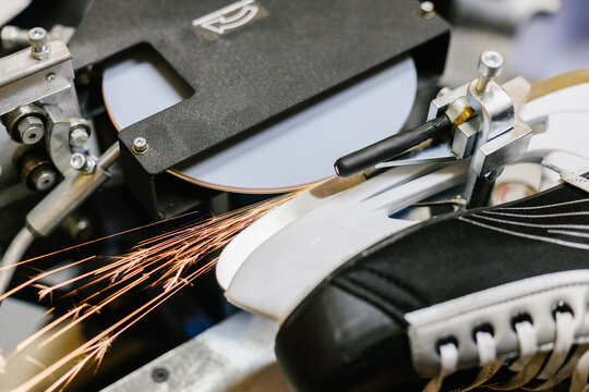 Grinding machine creating bright sparks while sharpening the metal blade of a black ice hockey skate.