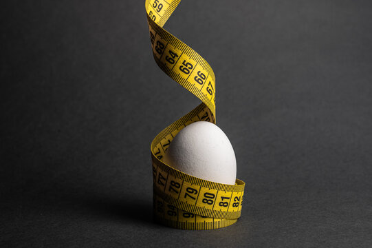 A white egg on a dark surface, wrapped in yellow tape, highlights nutrition and diet