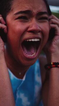 close-up of dark-skinned African American woman feeling stees, screaming in emotional agony while holding her headphones. raw vulnerability, showcasing intense frustration, pain, and inner turmoil
