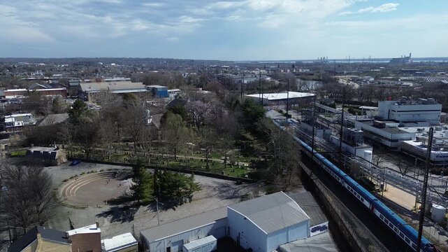 Rail corridor overlook rail line beside East Side cemetery frames industrial edge near E 7th St. Sunlit rooftops, tree clusters, rail textures, muted industrial surfaces in Wilmington, DE