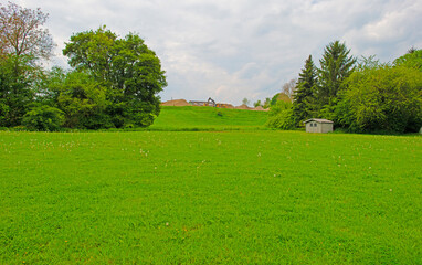 Fototapeta premium Fields and trees in a green hilly landscape under a cloudy blue sky in sunlight in springtime, Voeren, Limburg, Belgium, May, 2026
