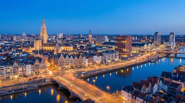 Panoramic view of the city of Antwerp at dusk, with its iconic cathedral and illuminated buildings along the river.