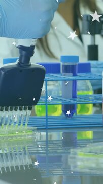 Vertical video: Gloved hand pressing pipette adding green into plate for lab with stars over hand
