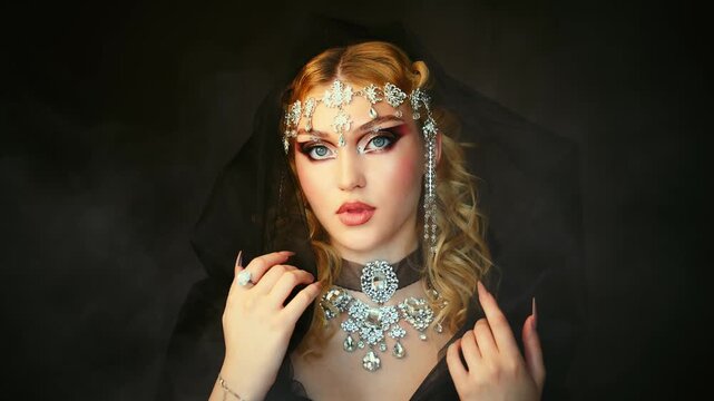Fantasy girl portrait dark queen woman beautiful face with art creative graphic makeup blue green eyes, luxury elf girl, black dress hood on head blonde long hair silver jewelry tiara crown diamonds.