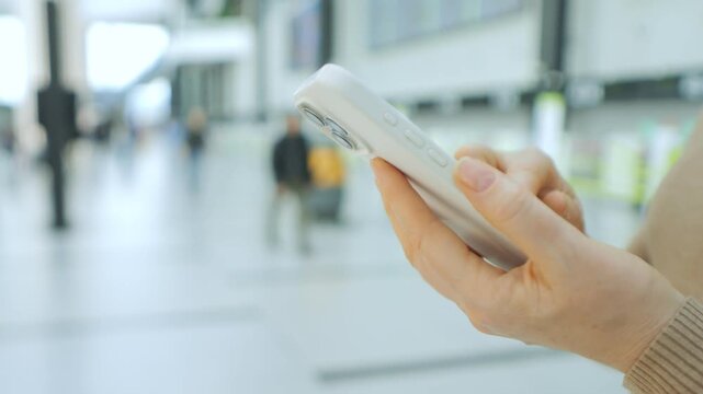 Hand holds smartphone in busy public space. Blurred background shows people walking. Focus remains on phone and hand only