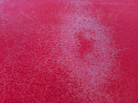 Macro close-up of a vibrant red textured surface with visible scratches and scuffs, ideal as an abstract background or material study for industrial and educational design projects.