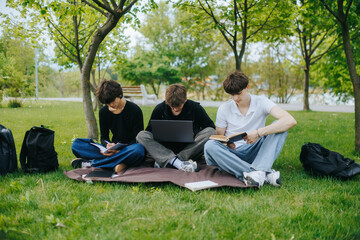 Three caucasian teenage boys studying on park grass with laptop and books © Alexandr