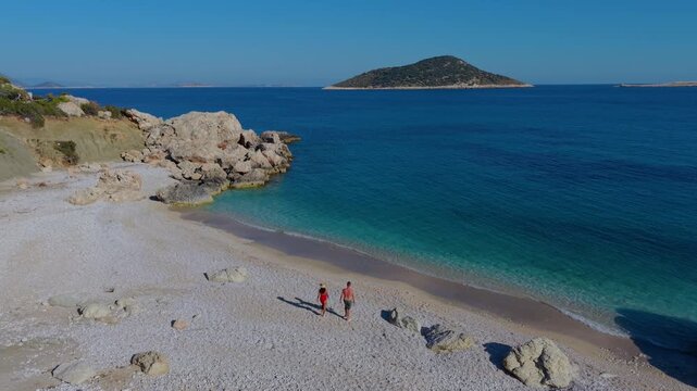 A couple wanders along the beautiful pebbled beaches of Kas, Turkey, enjoying the breathtaking turquoise sea. Perfect for relaxation and adventure