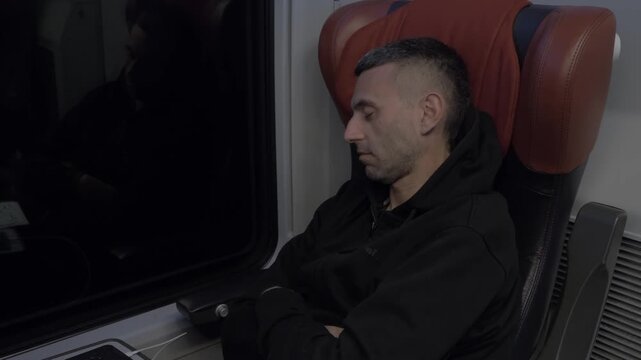 Young dark-haired man sleeping comfortably in a first class train seat during a quiet overnight journey.