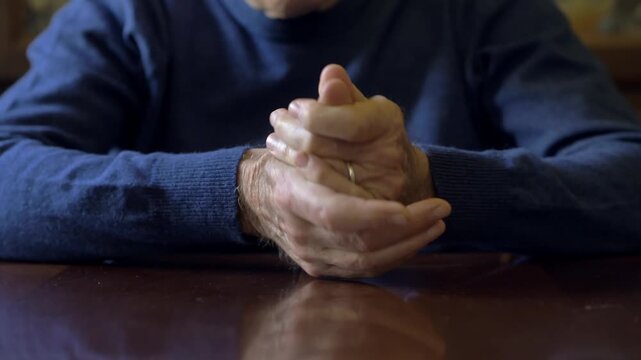 Elderly man hands slowly massage each other while dealing with chronic joint pain and physical discomfort inside a quiet domestic environment at home.