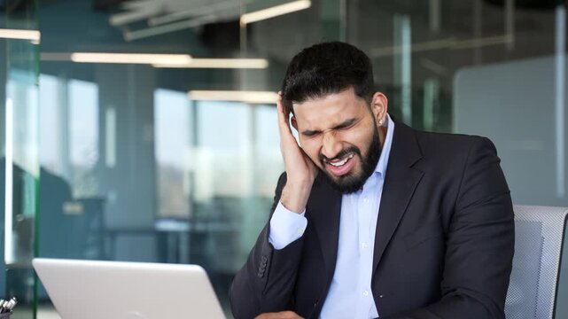 Unhealthy businessman in suit suffers from ear pain sitting in office. Sick male touches his ear with his fingers. He has furuncle, shingles, eczema, ear diseases or otitis media. Earache. Close up