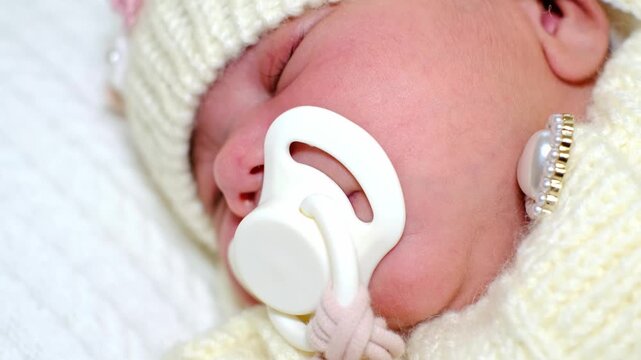 A slow tight macro close-up lingers on a sleeping newborn with a white pacifier, framed by cream knitwear and soft focus. It suits baby care, soothing routines, comfort, and family lifestyle.