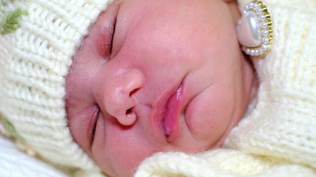 A tight macro close-up lingers on a sleeping newborn face, framed by cream knitwear, pearl details, and shallow focus. This footage suits baby care, first portraits, tenderness, and family lifestyle.