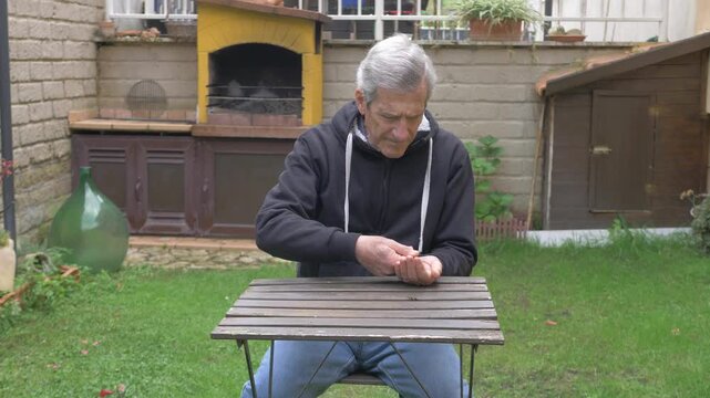 Mature man counting his last remaining coins at a garden table, conveying financial struggle and economic uncertainty.