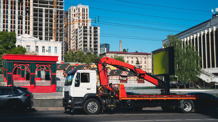 White industrial truck with a red hydraulic crane manipulator parked on a city street. Background features modern high-rise buildings under construction and historic architecture in Kyiv, Ukraine © Вита Курило