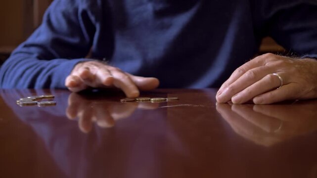 Hands of a mature man count a few coins on a home table, symbolizing financial difficulties, low pensions and economic hardship during difficult times.