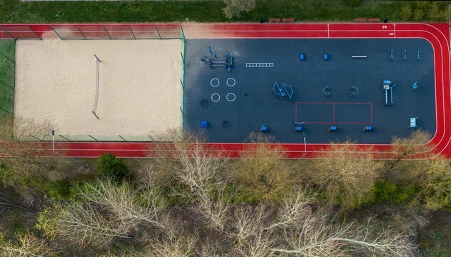 Aerial view of an outdoor sports complex with a red running track, sand volleyball court, and workout area near green trees Vilnius County, Lithuania.