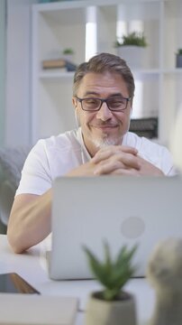Older man in white sitting at desk in bright room working with laptop computer in home office. Mature age, middle age, mid adult casual man in 50s, confident happy smiling.