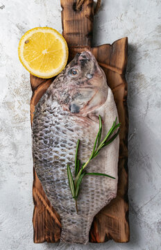 Fresh raw tilapia fish on a rustic wooden board with lemon and rosemary.