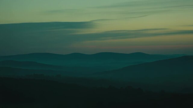 Layered mountains and ridges creating a tranquil scene at dawn with atmospheric mist filling the valleys and showcasing the beauty of a serene, expansive vista