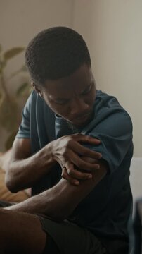 Vertical medium shot of young adult African American man pressing down patch on upper arm after inserting continuous glucose monitor during daily blood sugar management at home