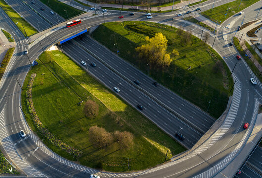 Aerial view of a multi-level highway interchange with traffic and a red bus driving on asphalt roads surrounded by green grass and trees in Vilnius County, Lithuania.