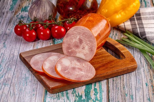 Sliced ham sausage on wooden cutting board with fresh cherry tomatoes and garlic