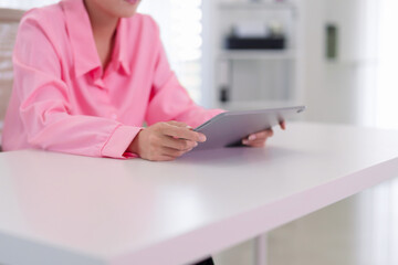 Asian business woman using digital tablet for online work browsing internet reading email at modern office desk wearing pink casual shirt professional © Pichsakul